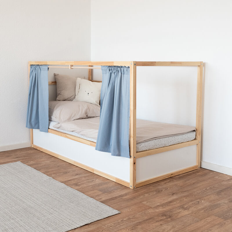 Seitenansicht eines Ikea Kura Betts mit aufgezogenen blauen Vorhängen, die an Holzstangen befestigt sind