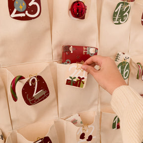 Ein Baumwollvorhang mit Taschen wird als Adventskalender genutzt. Eine Hand verziert die einzelnen Taschen mit Nummernkärtchen.