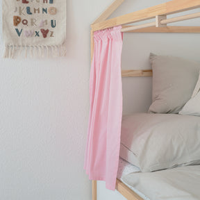 Teilansicht eines Kinderbetts mit einem rosa Vorhang der an hölzernen Vorhangstangen befestigt ist